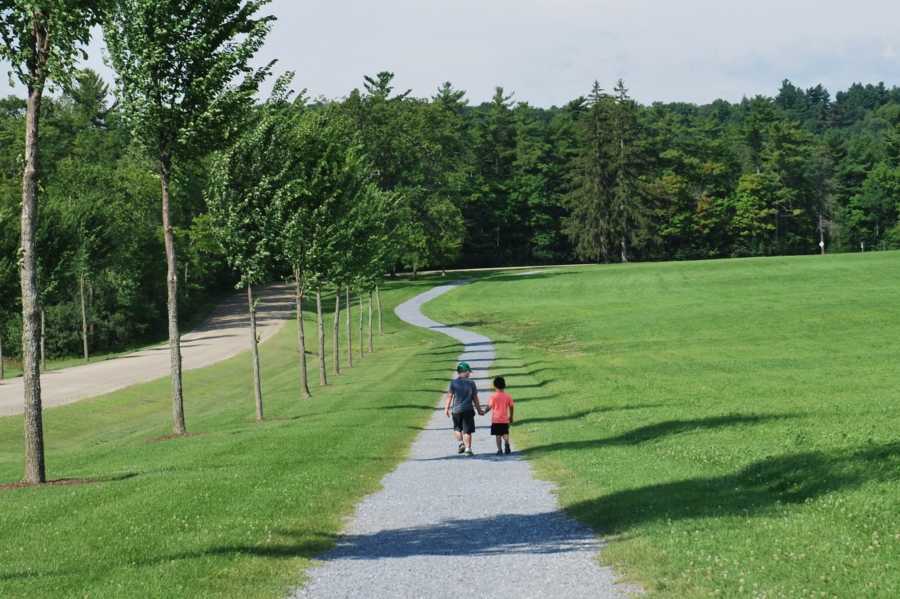 Children holding hands walking on trail next to large grassy area