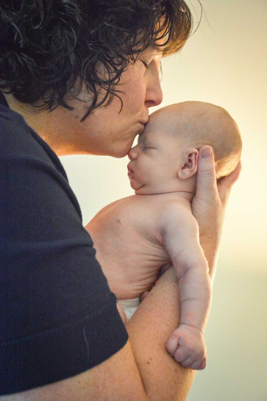 Mother who is shocked by how time flies so fast kissing forehead of newborn 