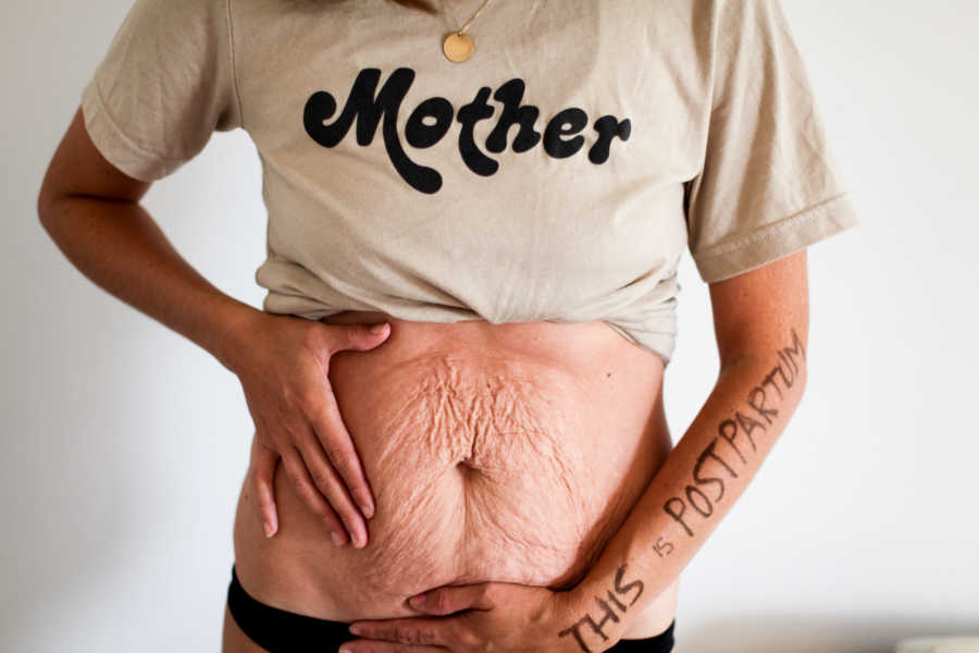 Mother who struggles with body image after pregnancy holds stomach that has extra skin