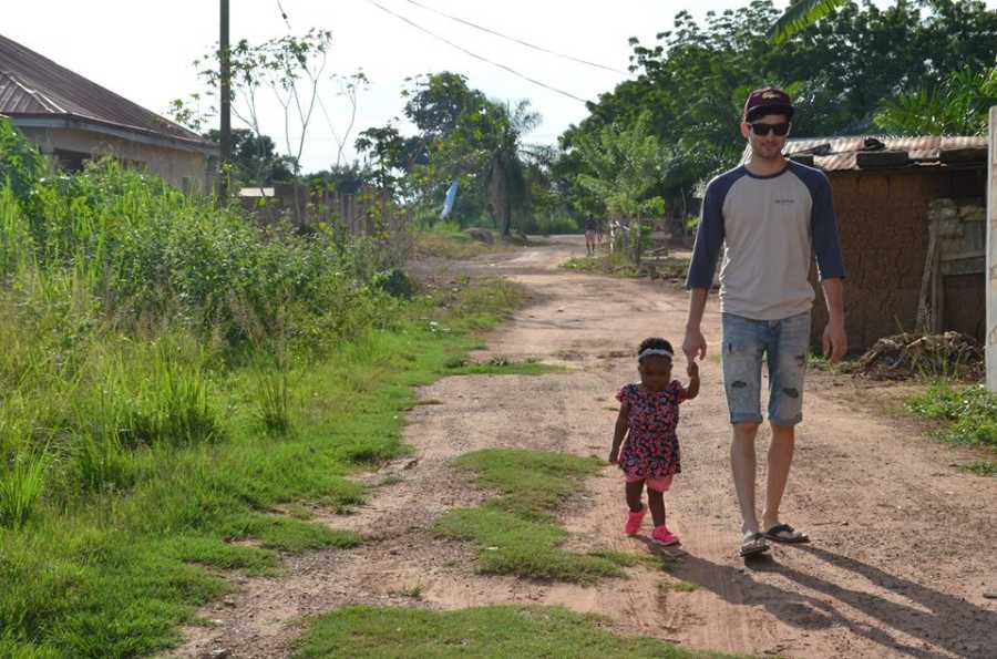 Father walks on dirt trail holding adopted daughter from Africa's hand