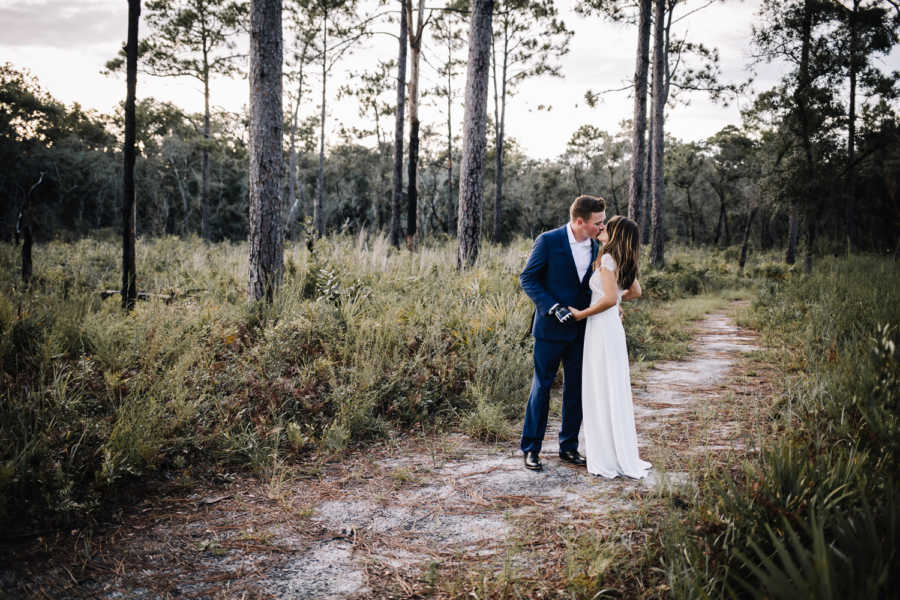 Bride and groom stand in field kissing 