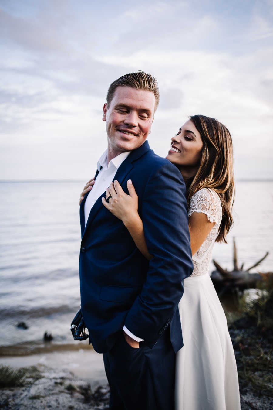 Bride stands holding groom from behind who has bionic hand