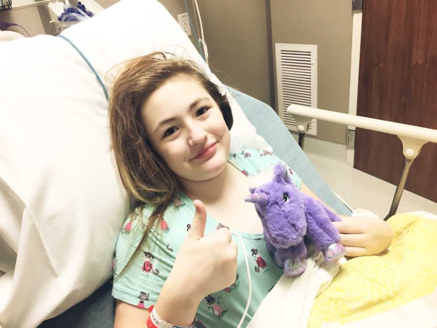 Ten year old with chronic appendicitis sits in hospital bed with thumbs up 