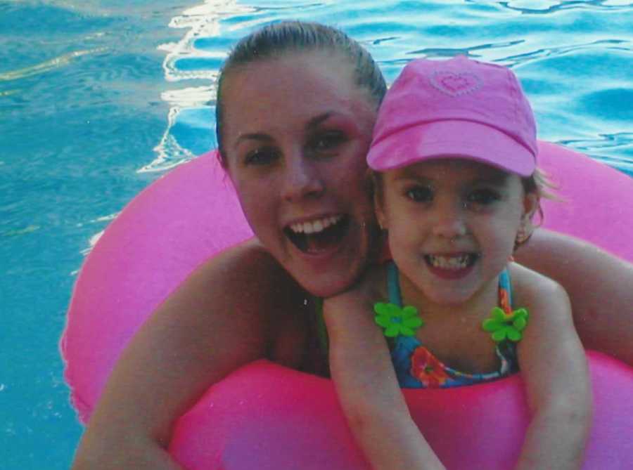 Young mother smiles in pink pool floaty with daughter