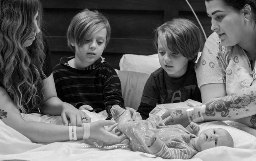 Woman sits beside her twin boys that sit next their mom's wife and their new child