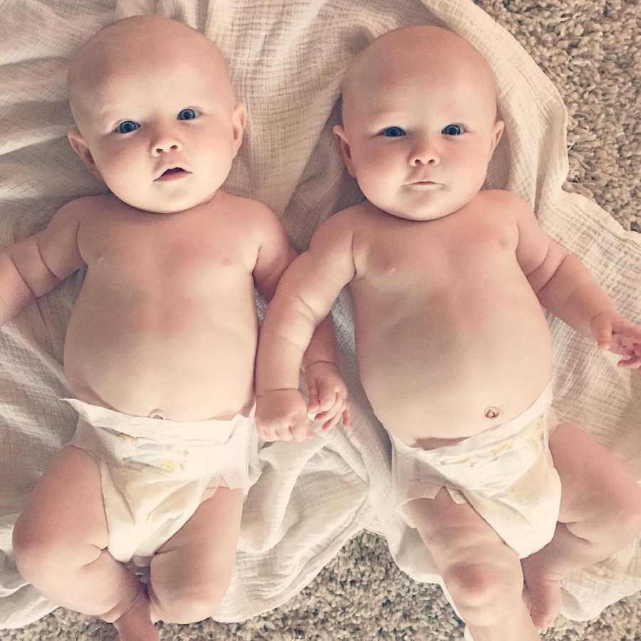 Baby twin girls lay on their back on blanket in their diapers