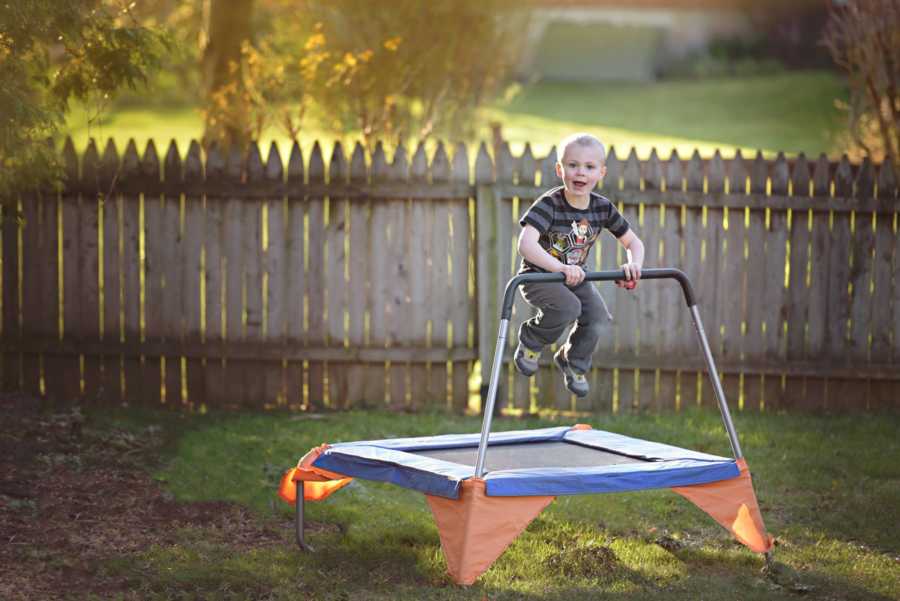Young boy with ADHD smiling as he bounces on trampoline in yard