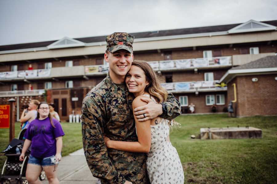 Army husband stands with arm around wife as he returns home from deployment