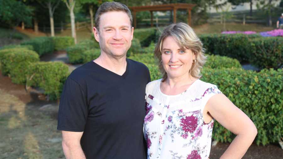 Husband and wife who lost lots of weight together stands arm in arm smiling outside