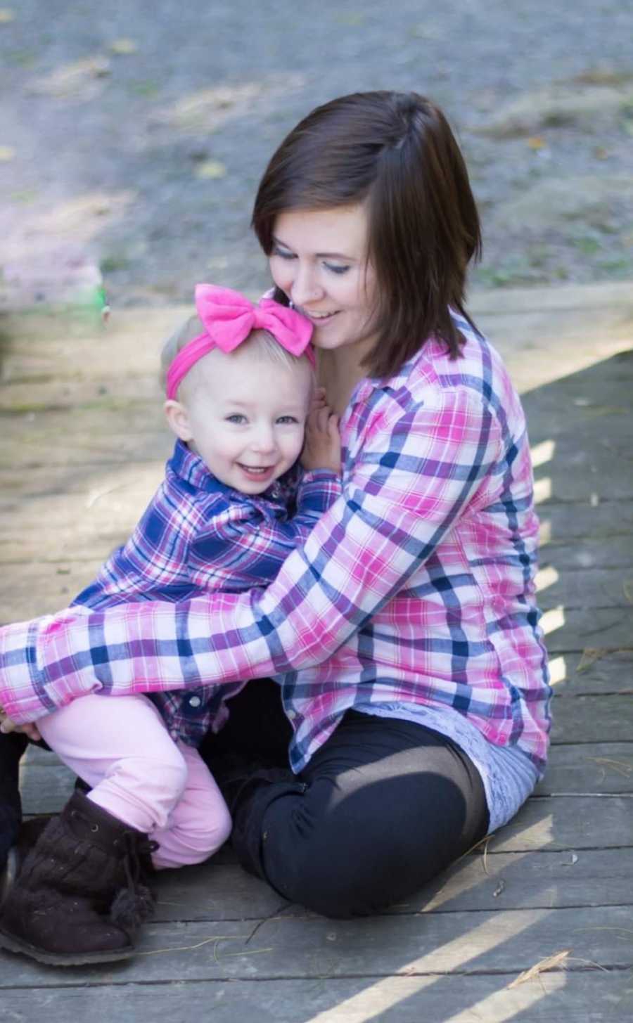 Woman who escaped abusive relationship sits on ground with toddler daughter smiling in her lap