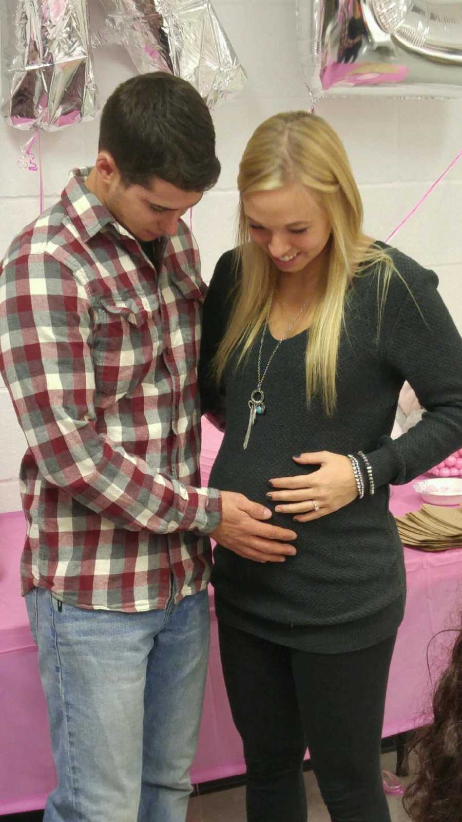 Pregnant woman stands beside husband as they both hold her stomach