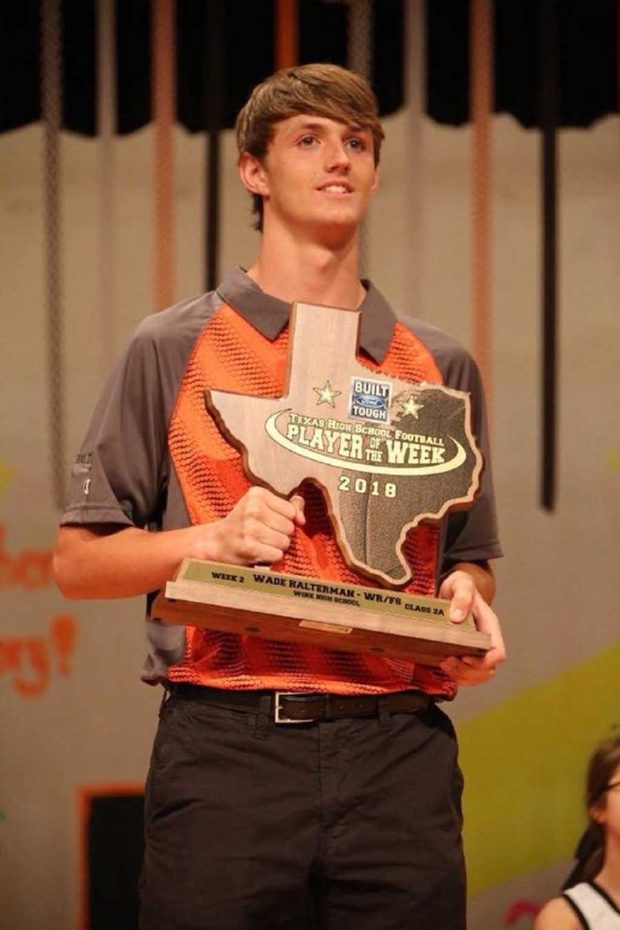 Teen stands holding trophy that says, "Texas High School Football Player of the Week"