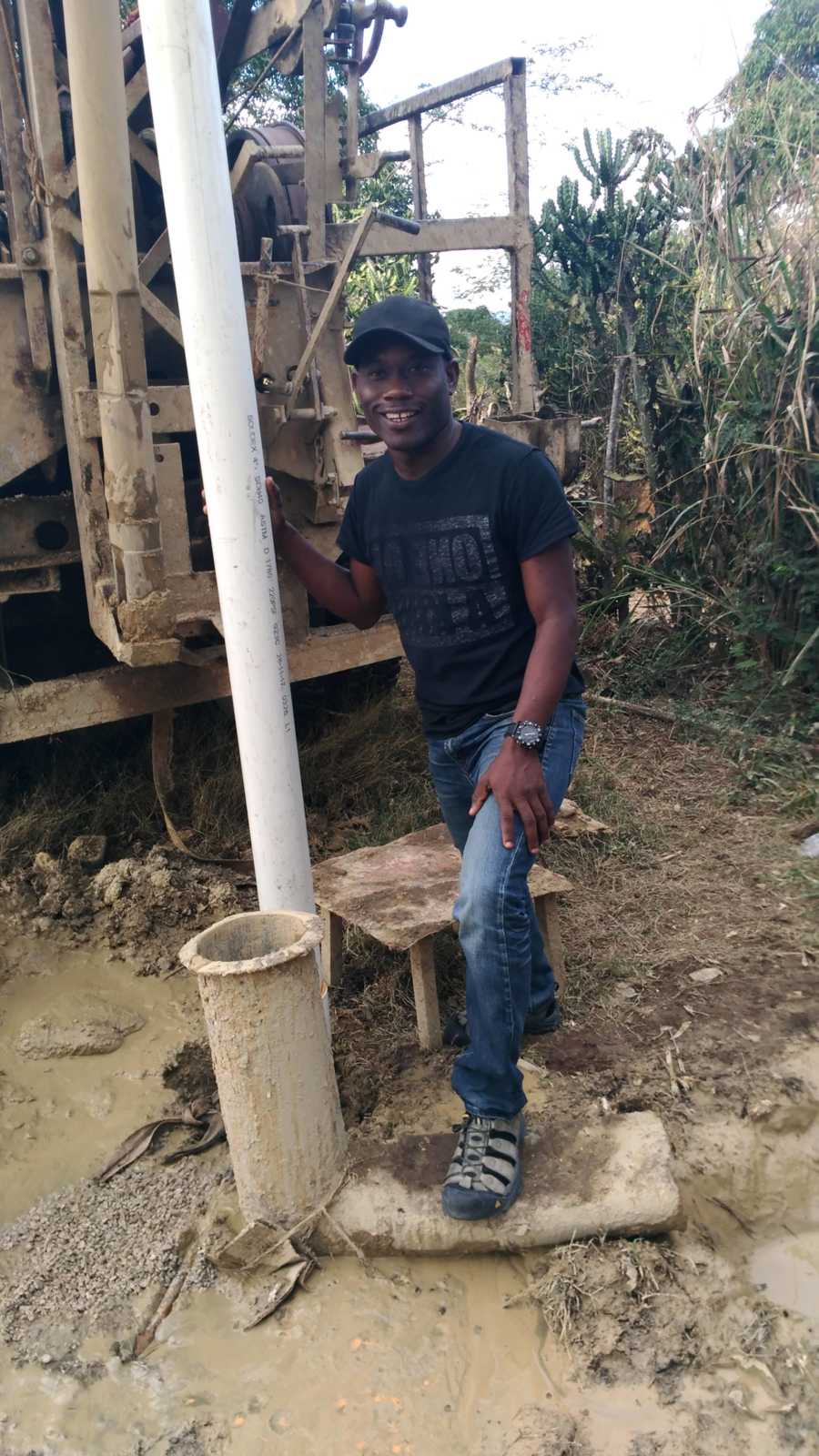 Man who fosters 62 children in Haiti stands in muddy area holding onto large PVC pipe