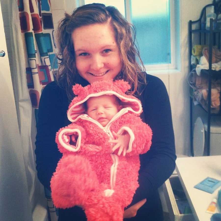 Mother smiles with newborn in pink fuzzy onesie sitting in her lap