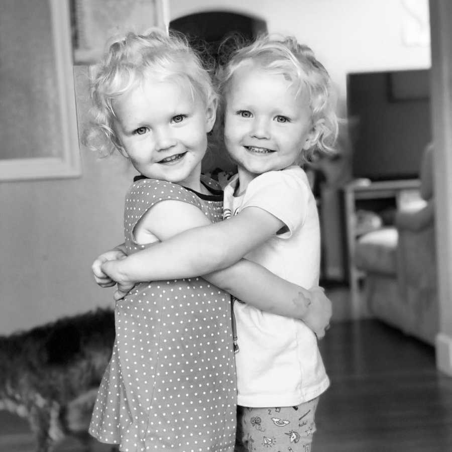 Twin girls smile as they hug each other in home