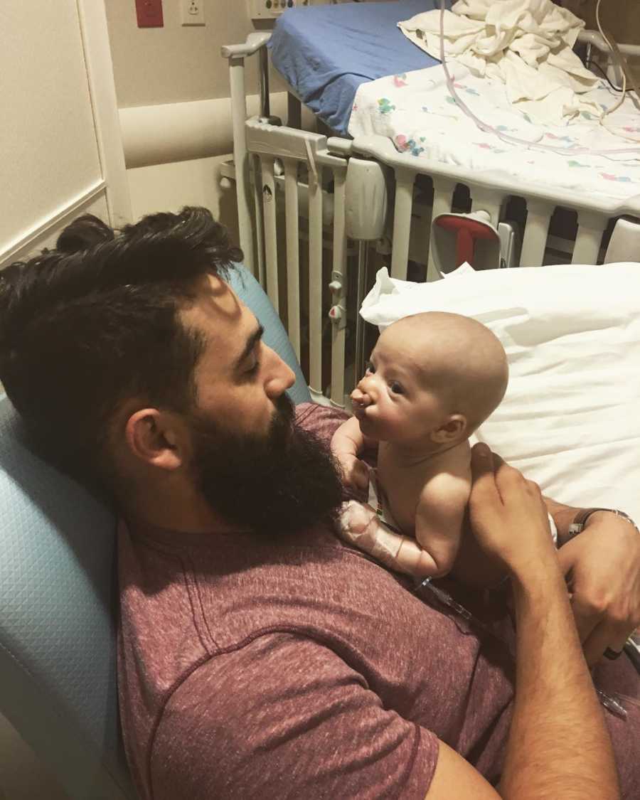 Father sits in hospital with son who had cleft palette surgery lying on his stomach