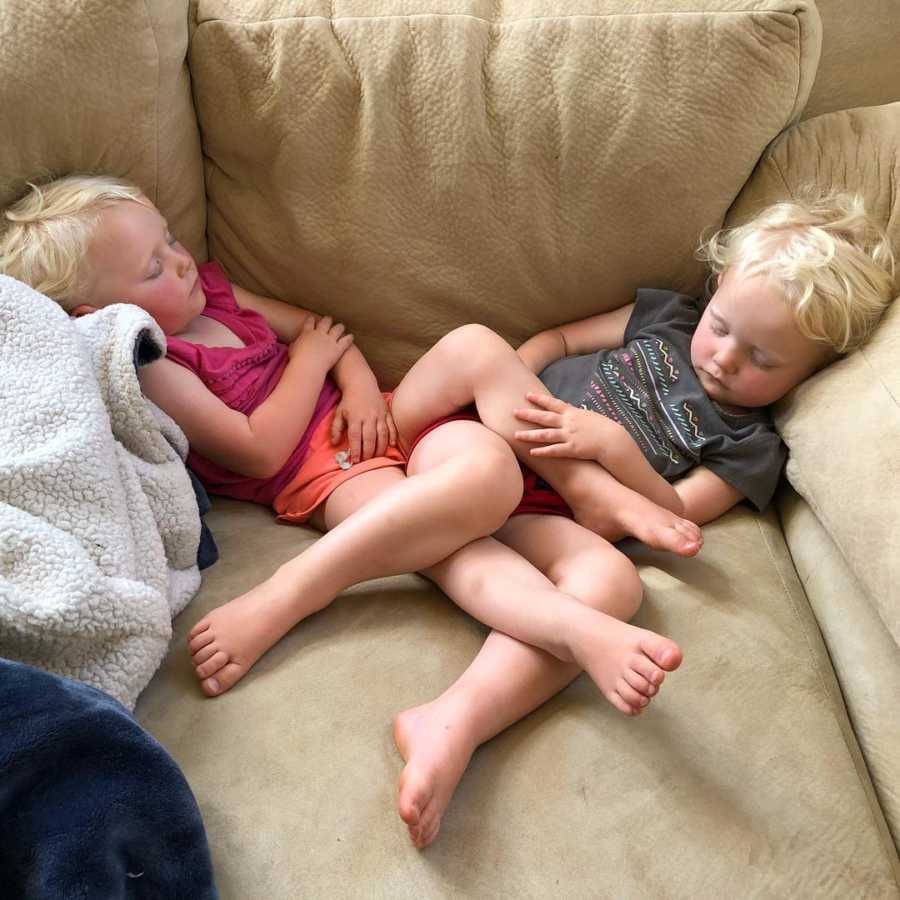 Twin girls sleep on couch with their legs intertwined