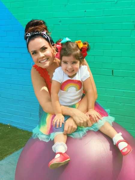 Mother who had a hard time leaving her child at school smiles behind her daughter while she sits on ball