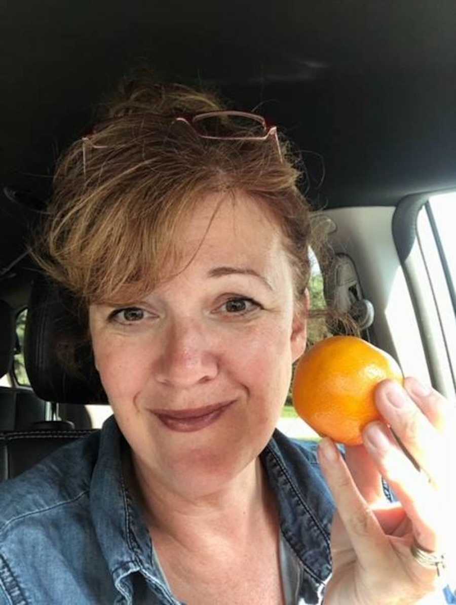 Woman smiling in selfie in her car while holding orange