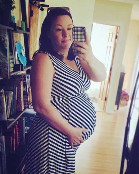 Pregnant woman with Factor V Leiden’s stands smiling in mirror selfie while holding her stomach