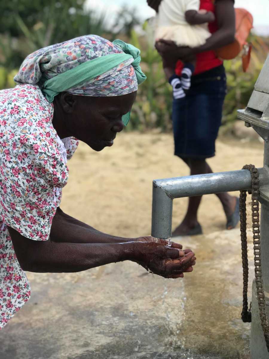 Haitian woman holds her hands under water pipe to wash her hands