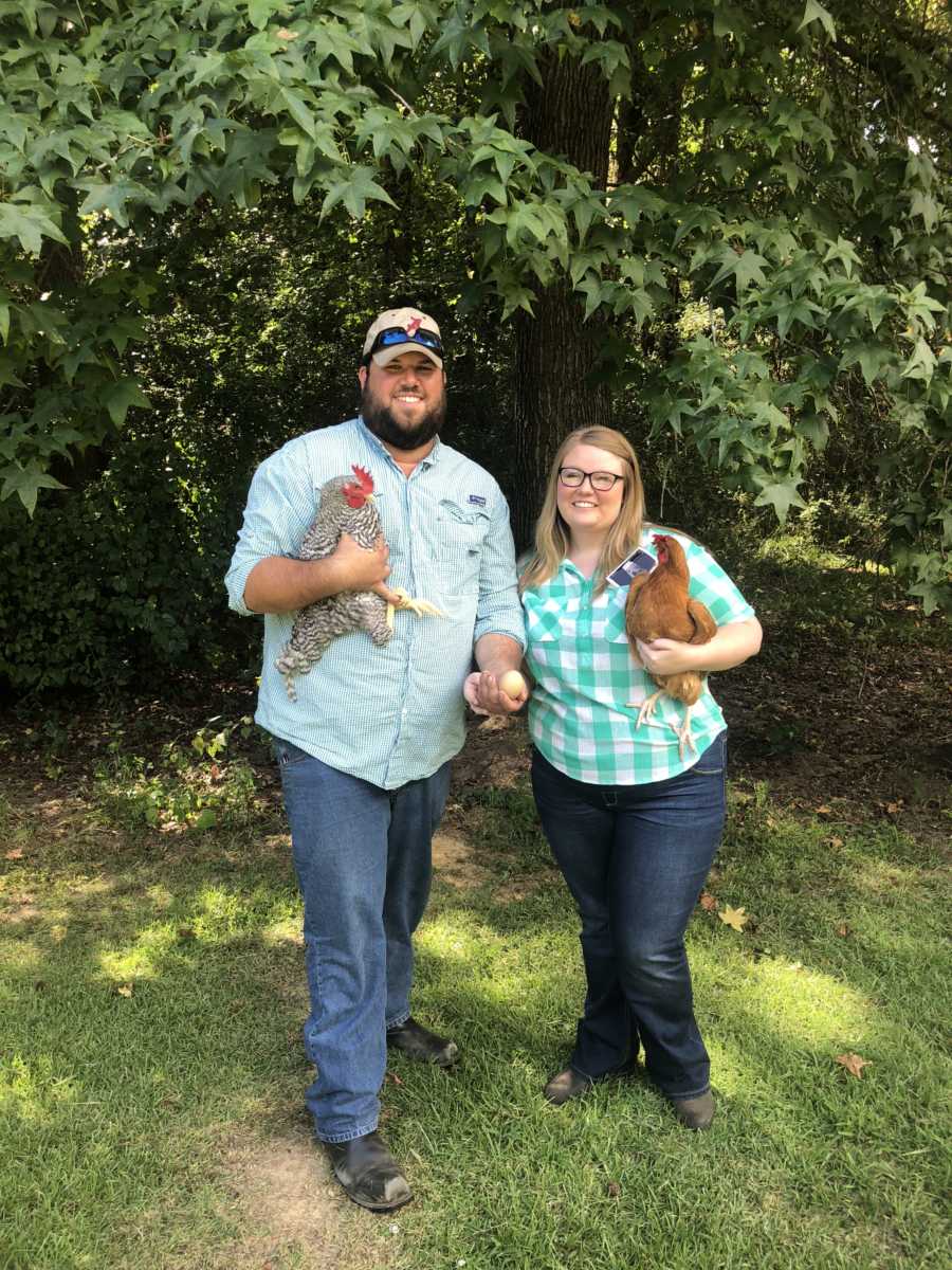 Husband and wife stand outside holding chickens in their arms