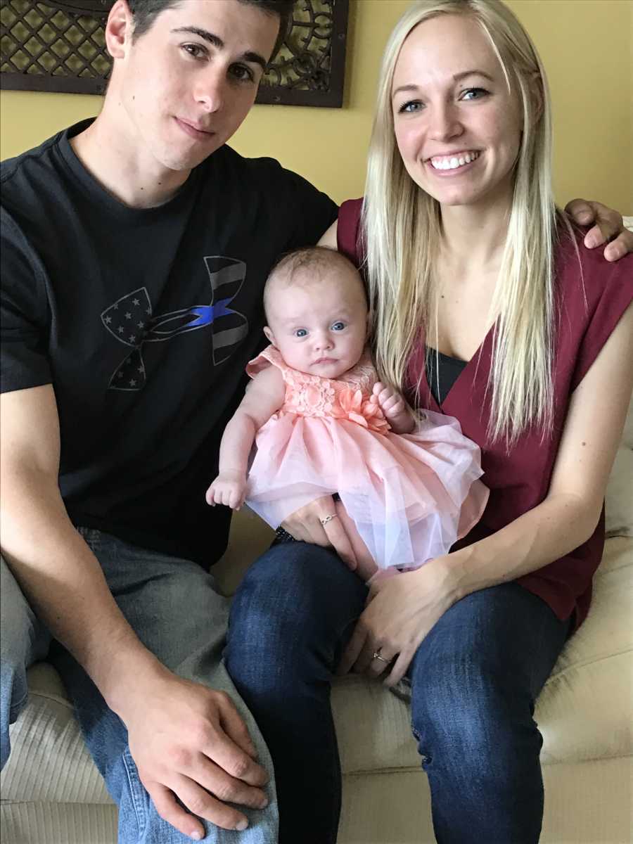 Husband and wife sit on couch while baby sits in wife's lap