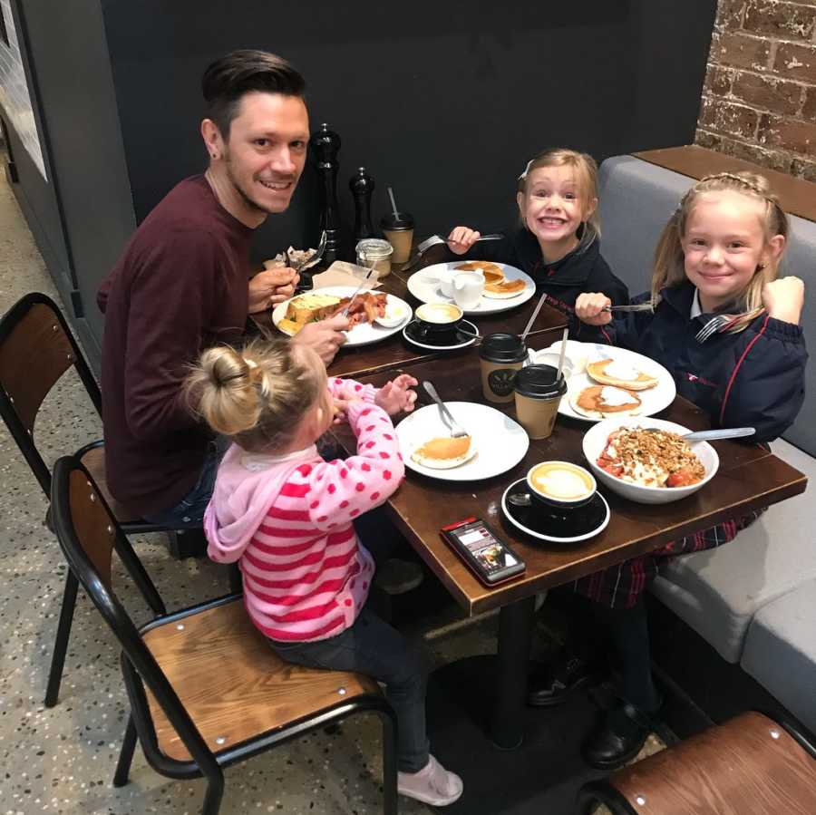 Father sits at restaurant table smiling with his three daughter's whom he has custody over