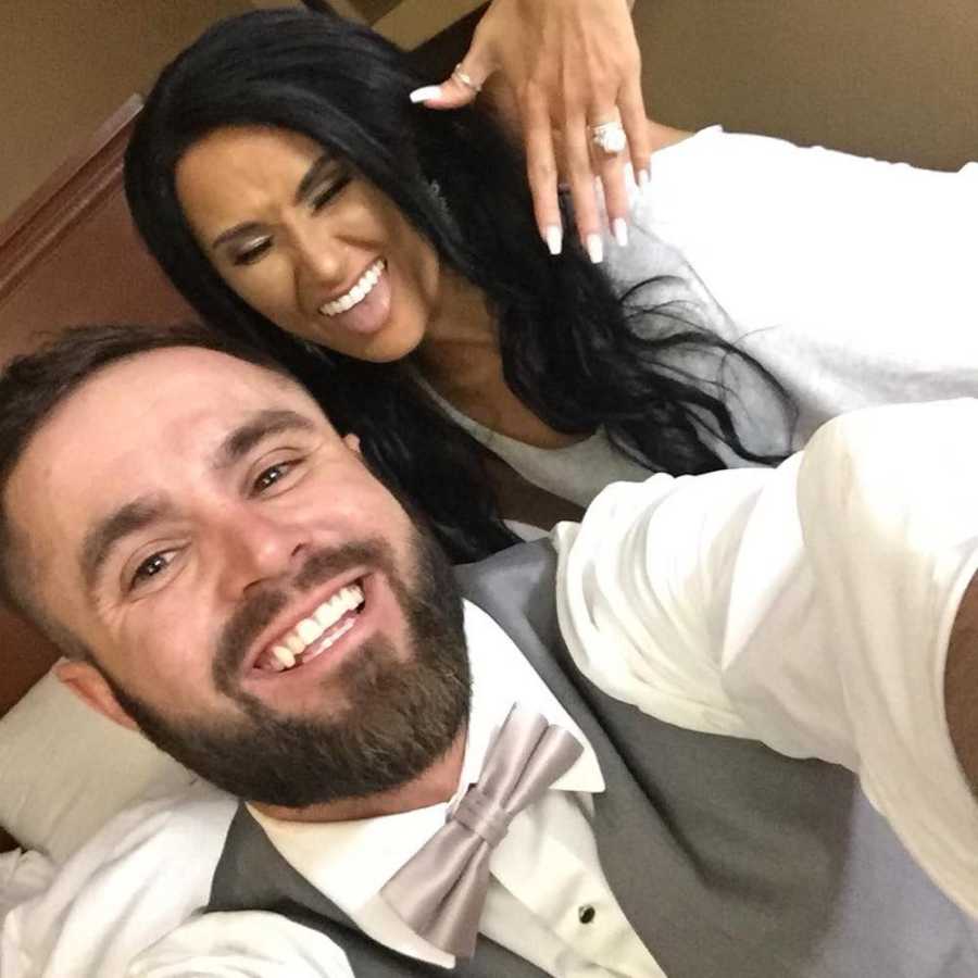 Groom smiles in selfie beside his bride who is holding out her hand to show rings