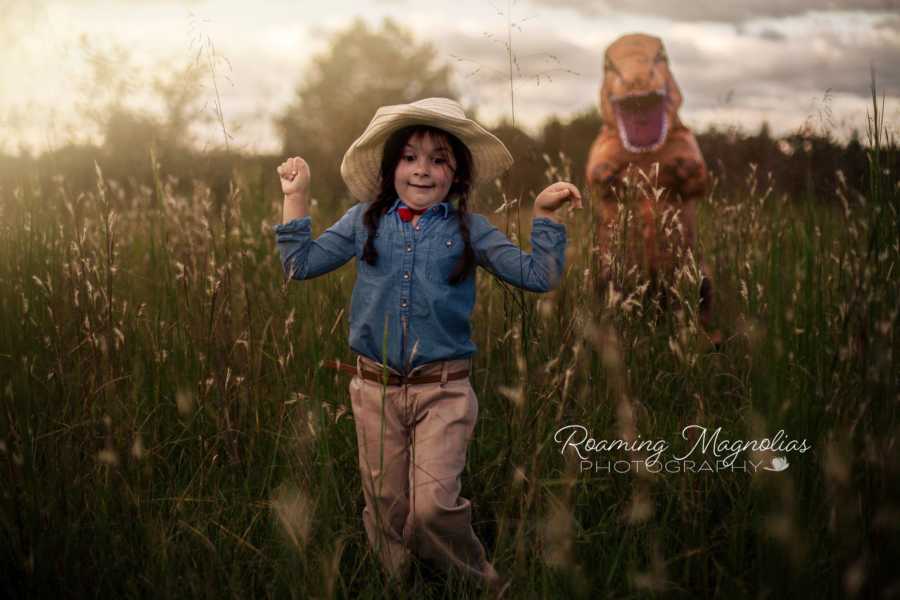 Young girl with autism is running in field away from dinosaur