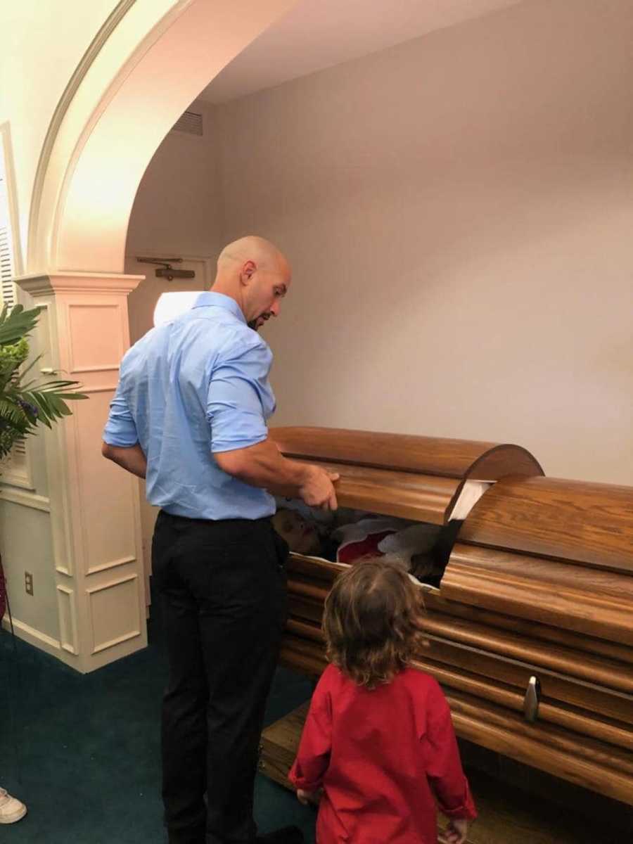 Man stands beside young son as he opens his wife's casket at funeral