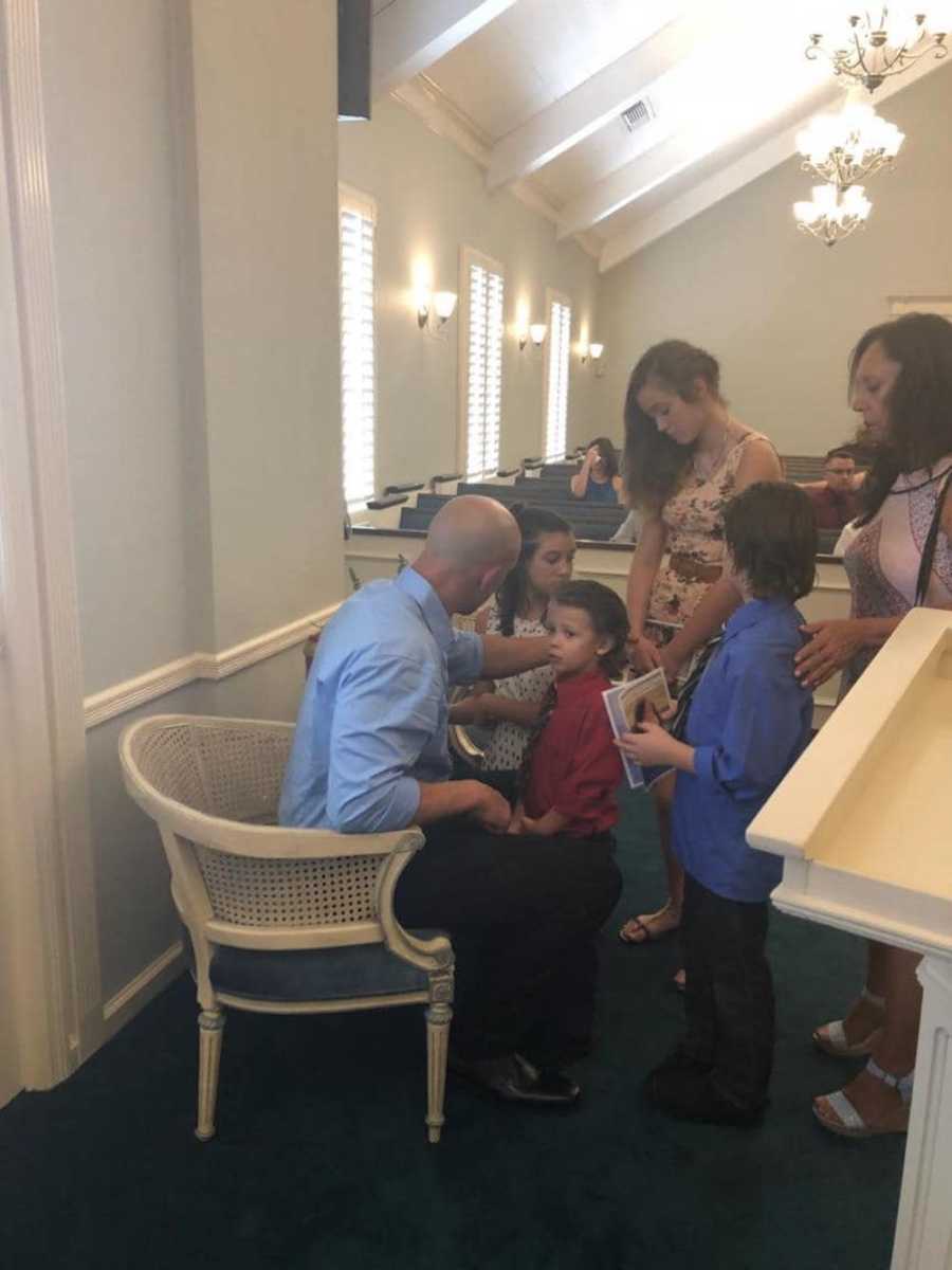 Father sits in chair consoling his children at his wife and daughter's funeral