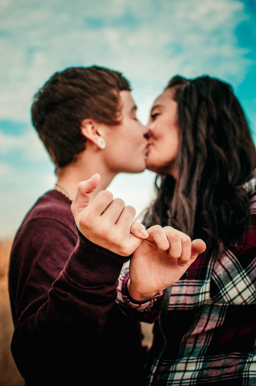 Girlfriend and transgender boyfriend kiss while interlocking their pinkies