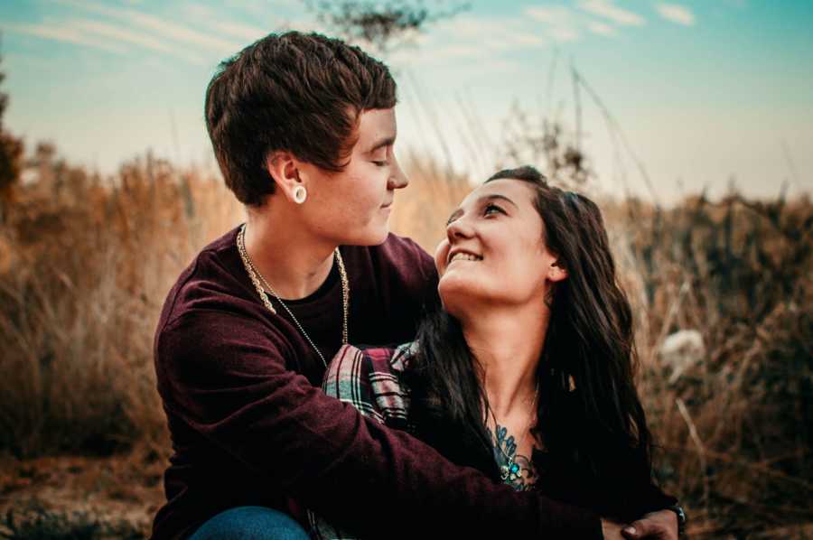 Transgender boyfriend holds arms around girlfriend who is smiling up at him