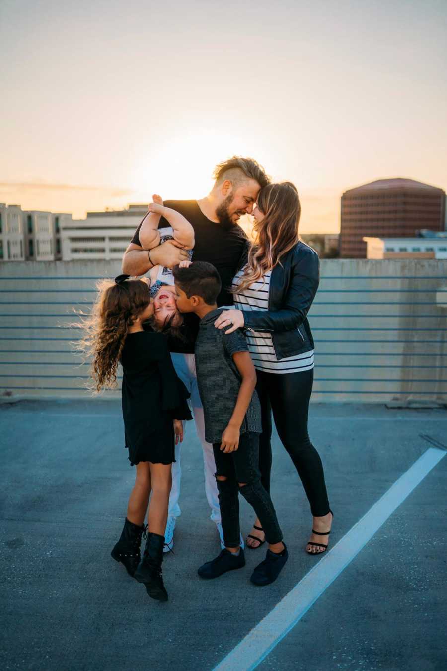 Woman stands on top of parking garage with her two children, boyfriend, and his daughter