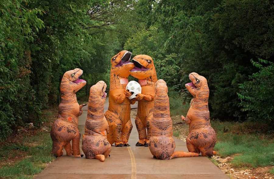 Family of 6 stand in road dressed in dinosaur costumes for baby announcement
