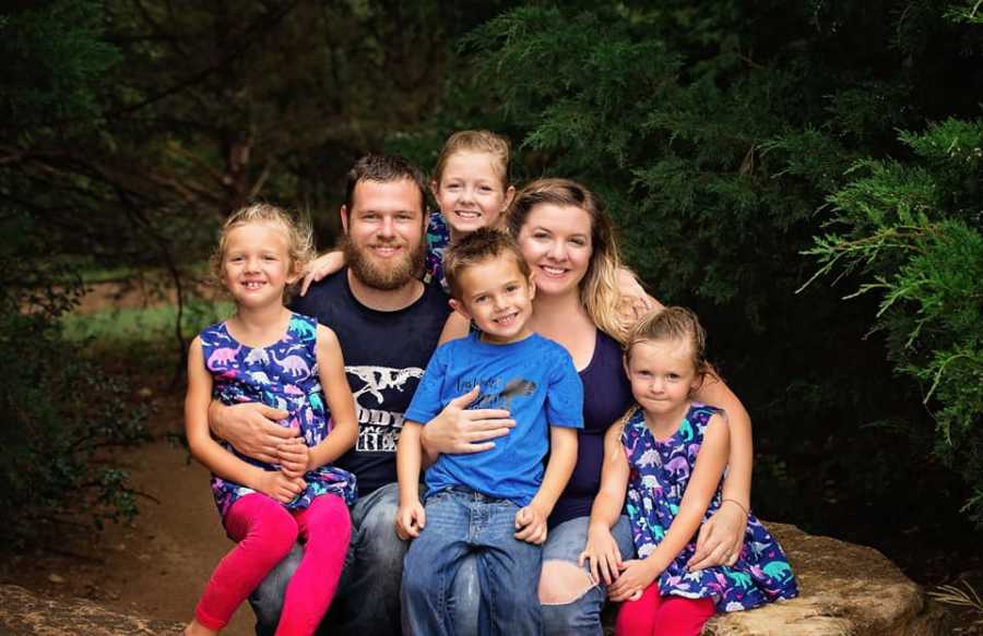 Husband and wife sit on rock with their four children in their laps