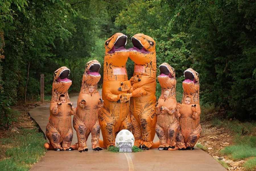 Family in dinosaur costumes stand in street with egg in front of them for baby on the way