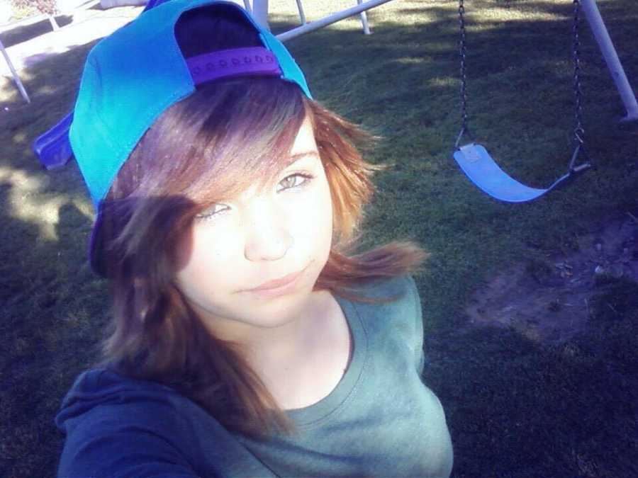 Teen lesbian wearing blue backwards hat in selfie near swing set