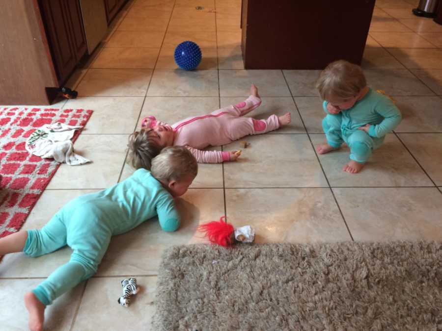 Two triplets lay on floor of kitchen while third squats on floor