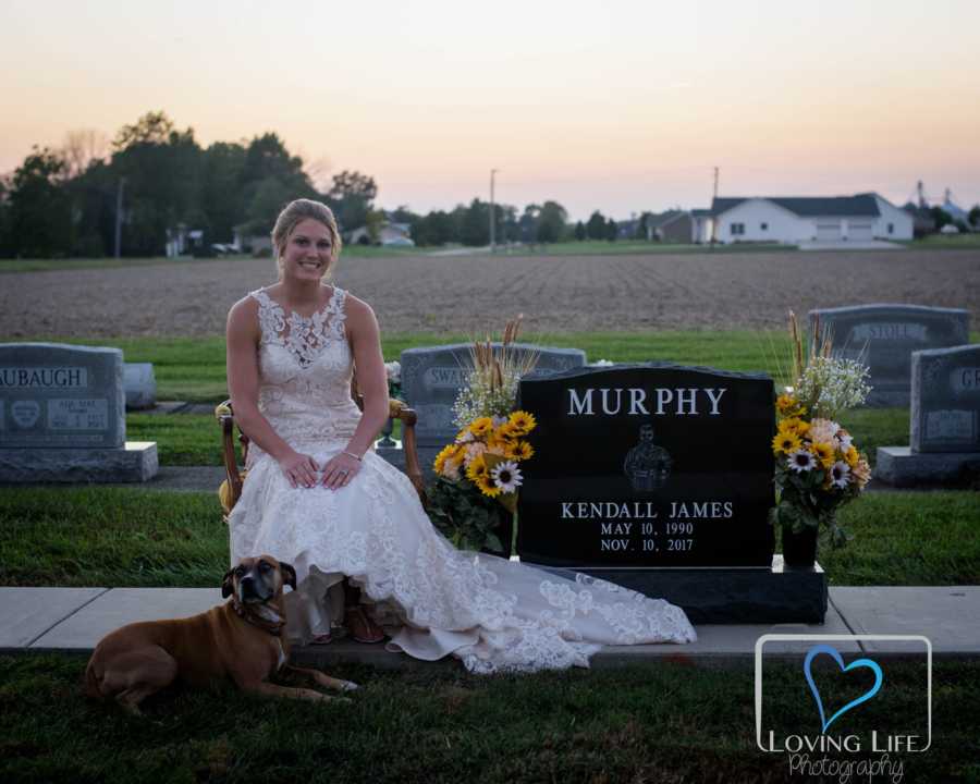 Woman in wedding gown sits beside late fiancee's head stone beside their dog