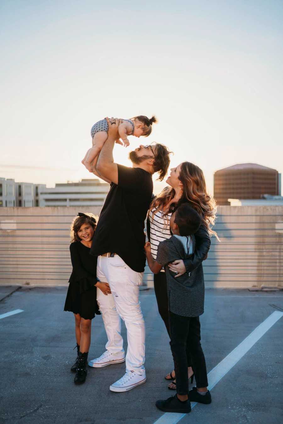 Woman stands with her son beside her boyfriend who is holding up his daughter beside her daughter
