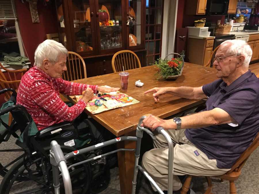 Elderly woman with dementia sits at kitchen table beside husband