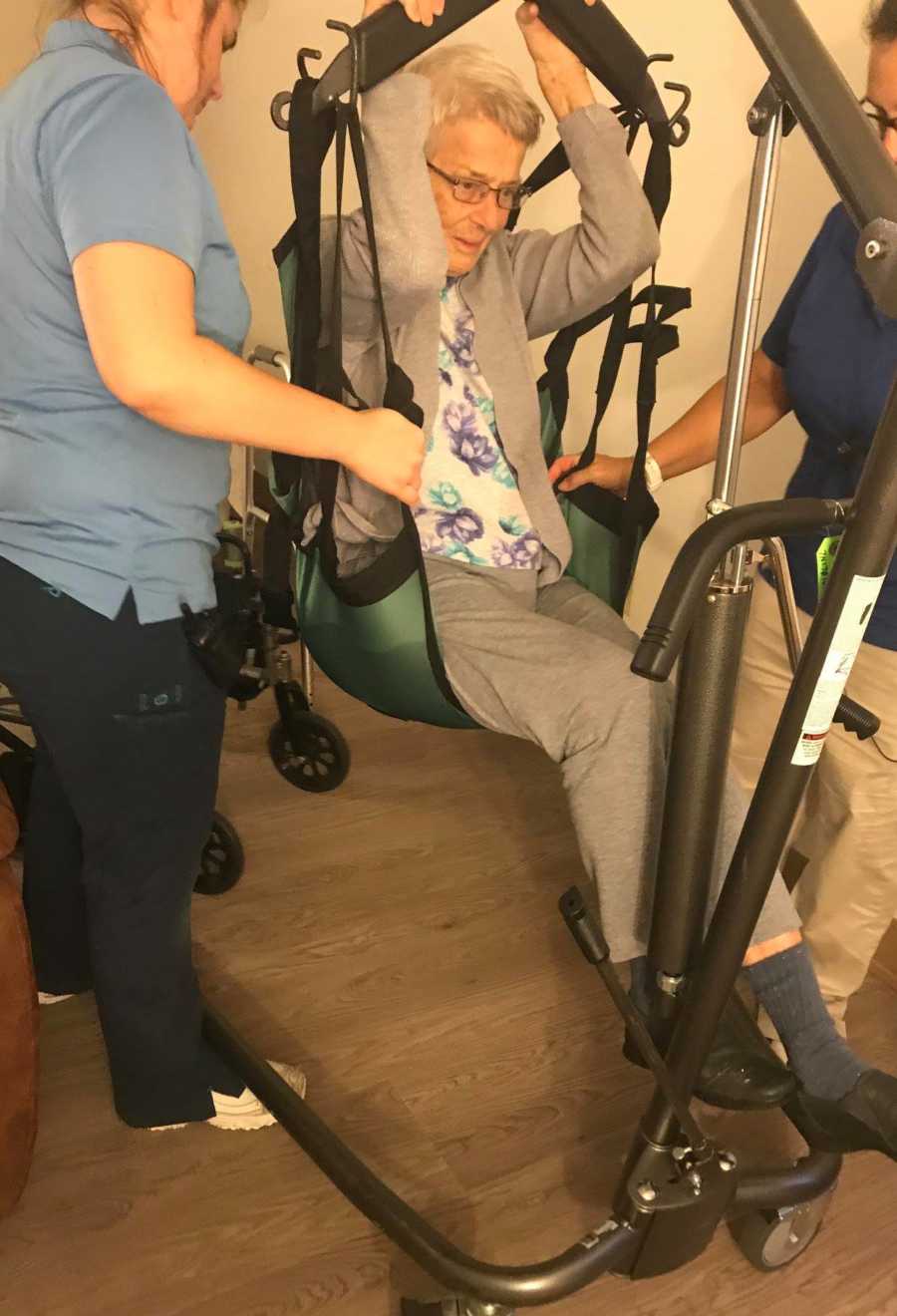 Elderly woman with dementia sits in physical therapy machine with helpers