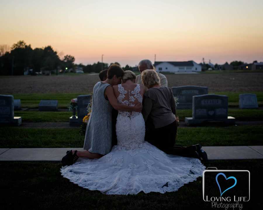 Woman in wedding gown kneels in front of late fiancee's headstone with his parents and hers