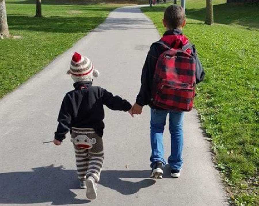 Older brother holds younger brother's hand as they walk on path 
