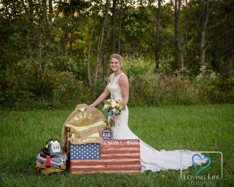 Woman stand in wedding gown beside late fiancee's fireman's uniform and American Flag