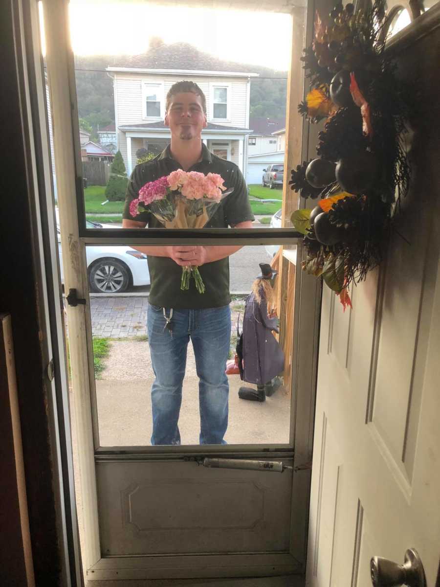 Man standing outside of front door holding bouquet of flowers