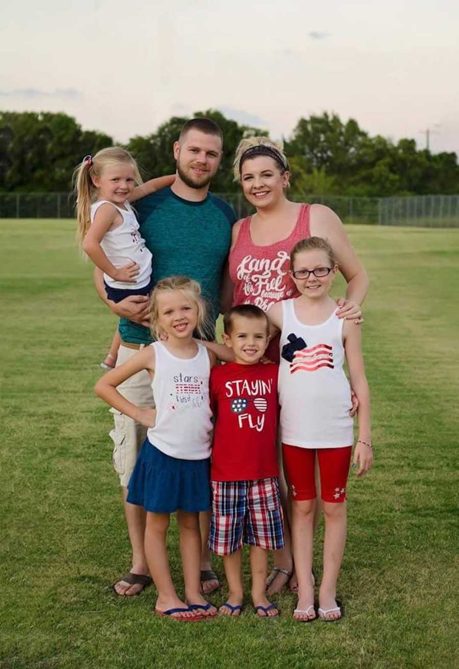 Husband and wife smile outside standing beside four children