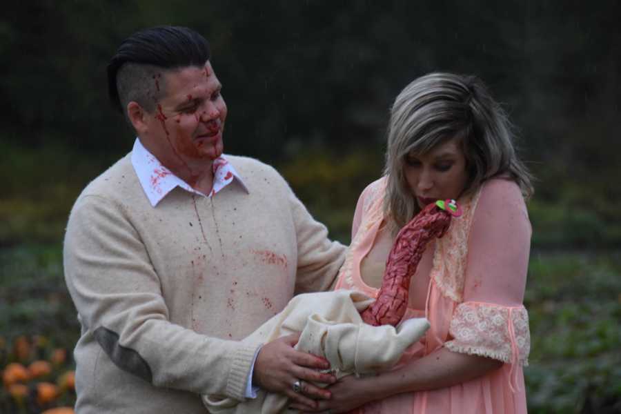Husband stands behind wife who kisses bloody creature that came out of her stomach